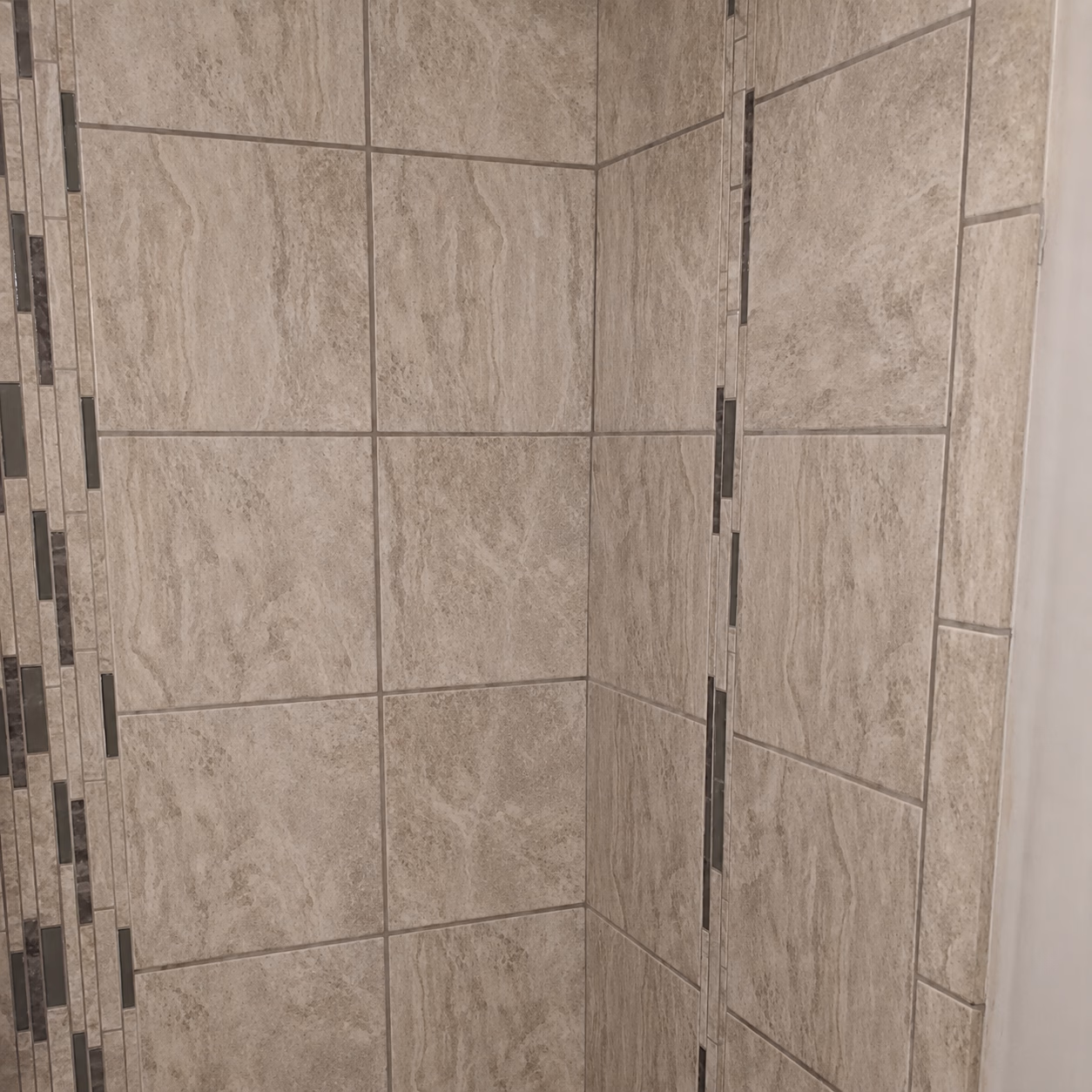 Corner wall with beige stone tiles accented by vertical strips of smaller dark mosaic tiles.