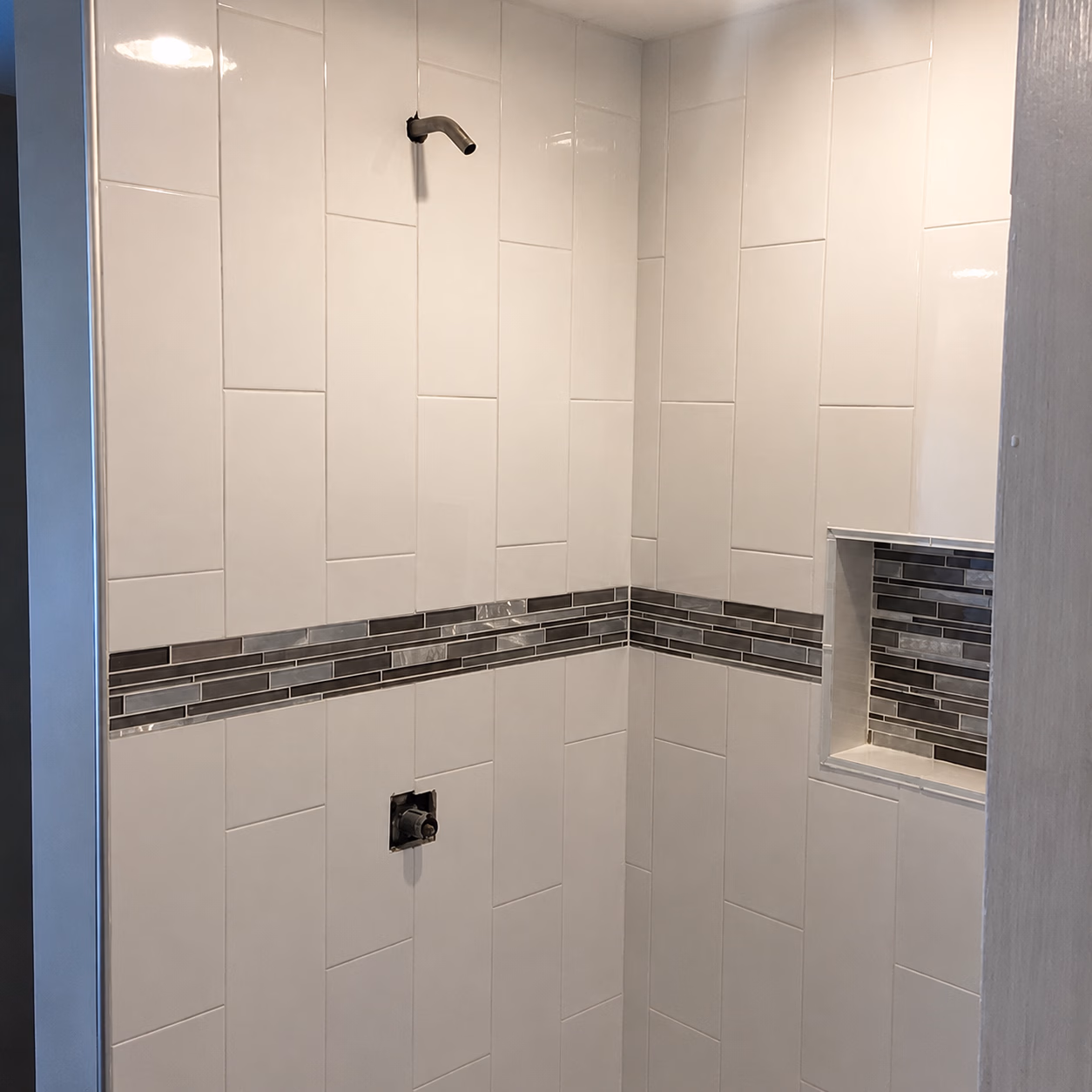 Tiled shower corner with white tiles, dark glass tile accent strip, and built-in niche.