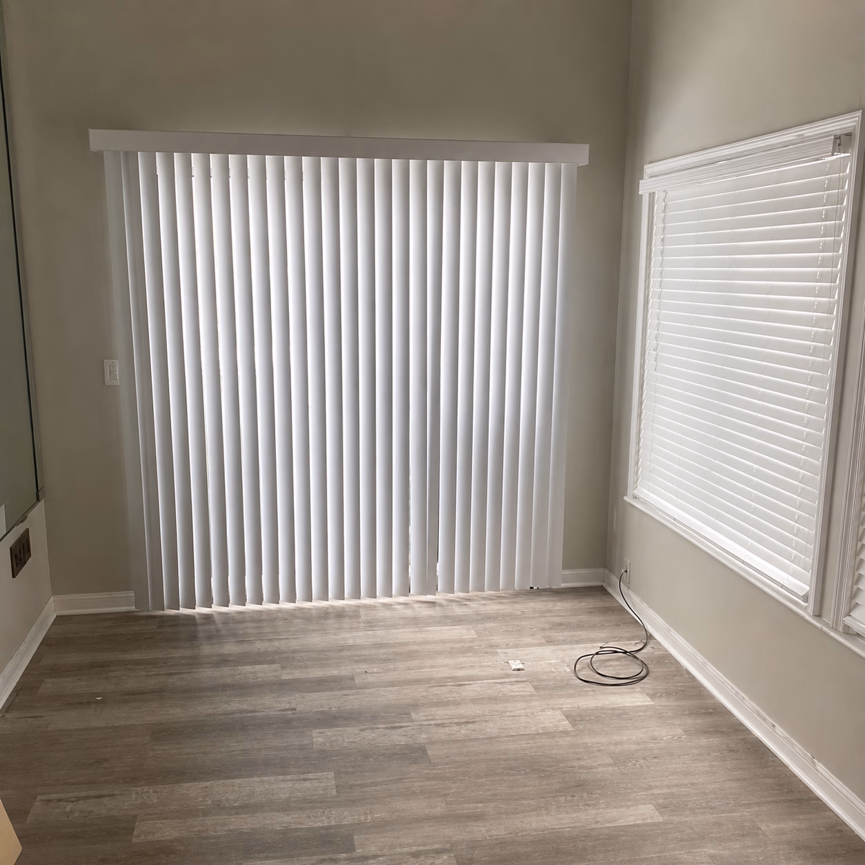 Empty room with light wood floors, white walls, vertical blinds, and a window with horizontal blinds.