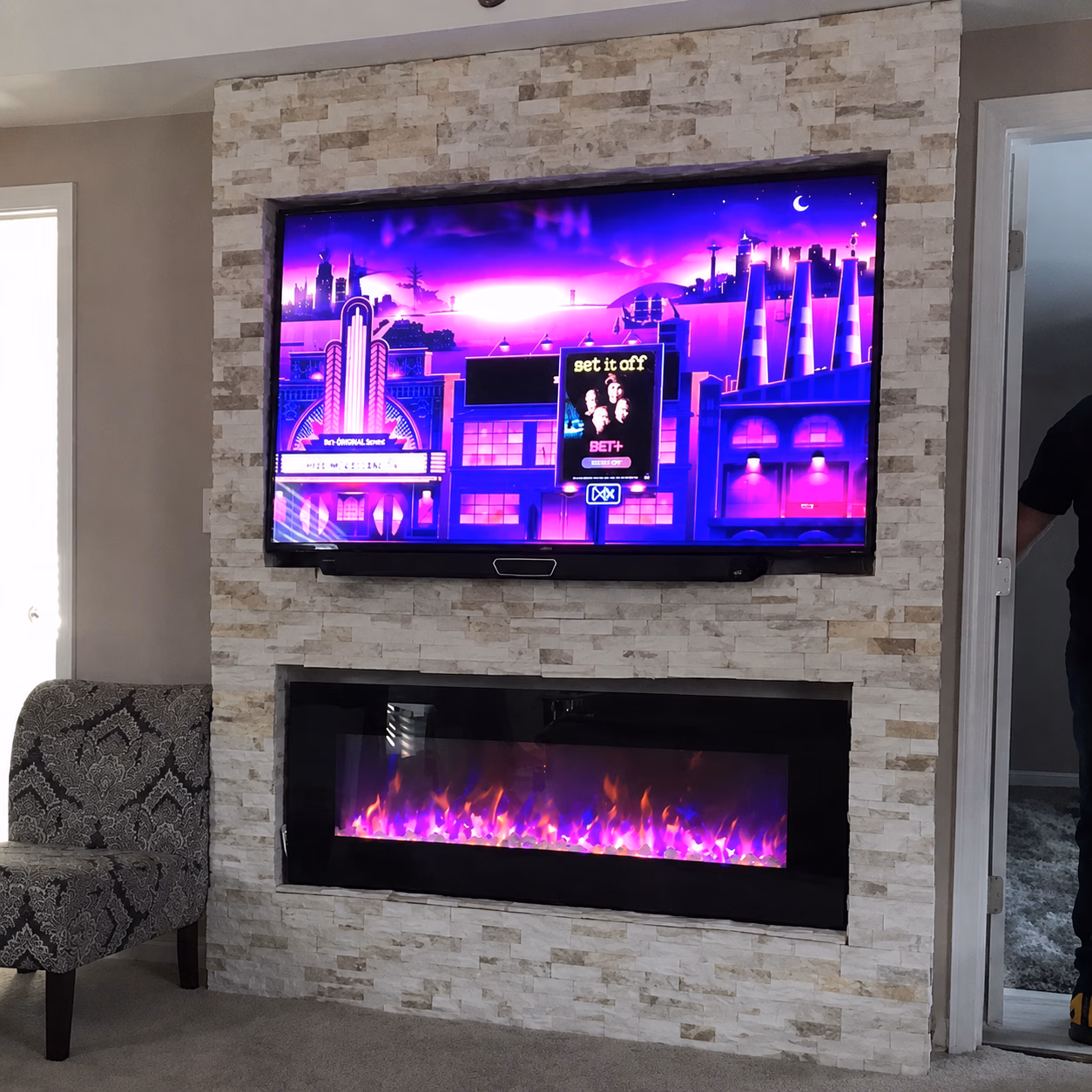 Modern stone fireplace with purple flames below a wall-mounted TV showing a purple cityscape animation.