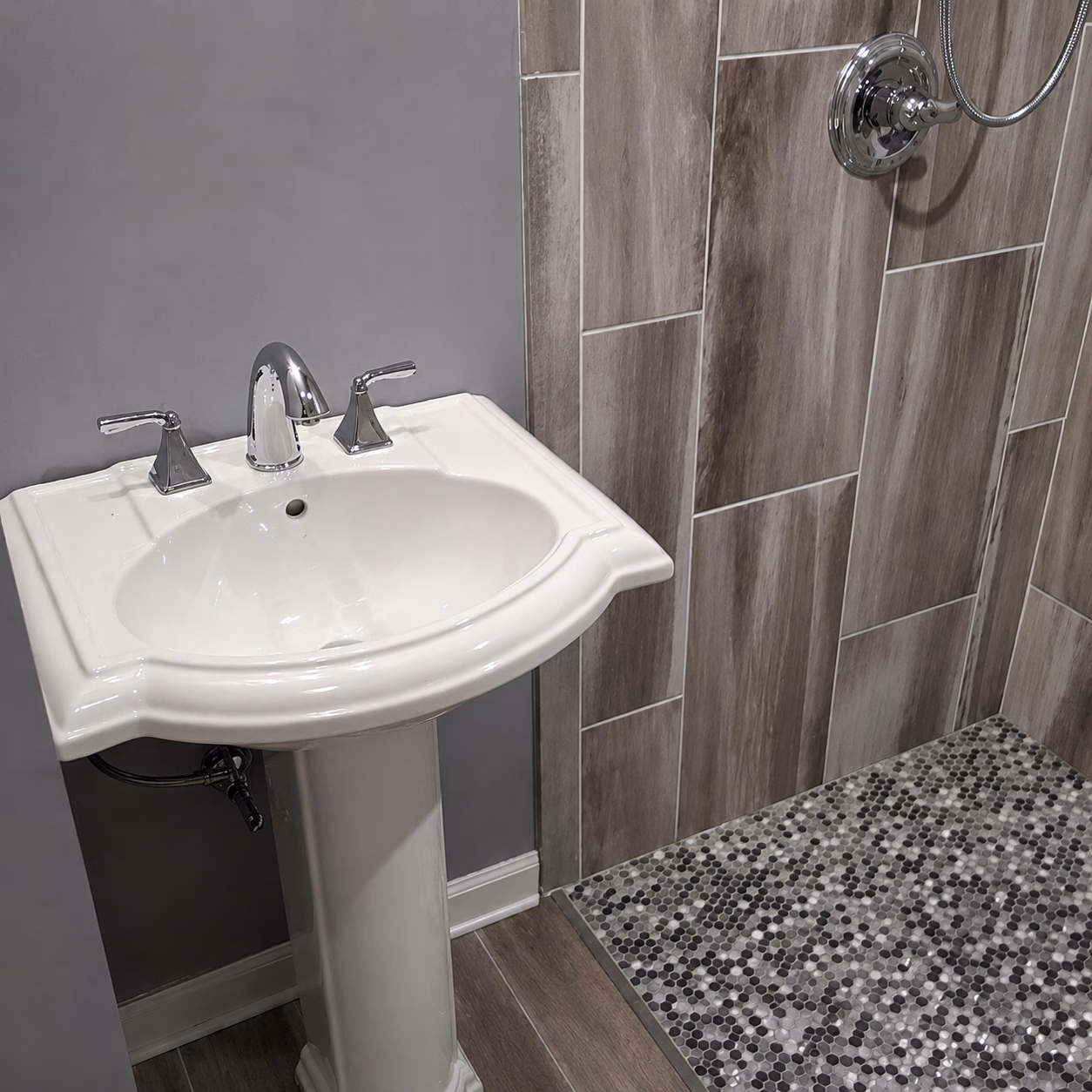 White pedestal sink with chrome faucet next to a tiled shower with pebble mosaic floor.