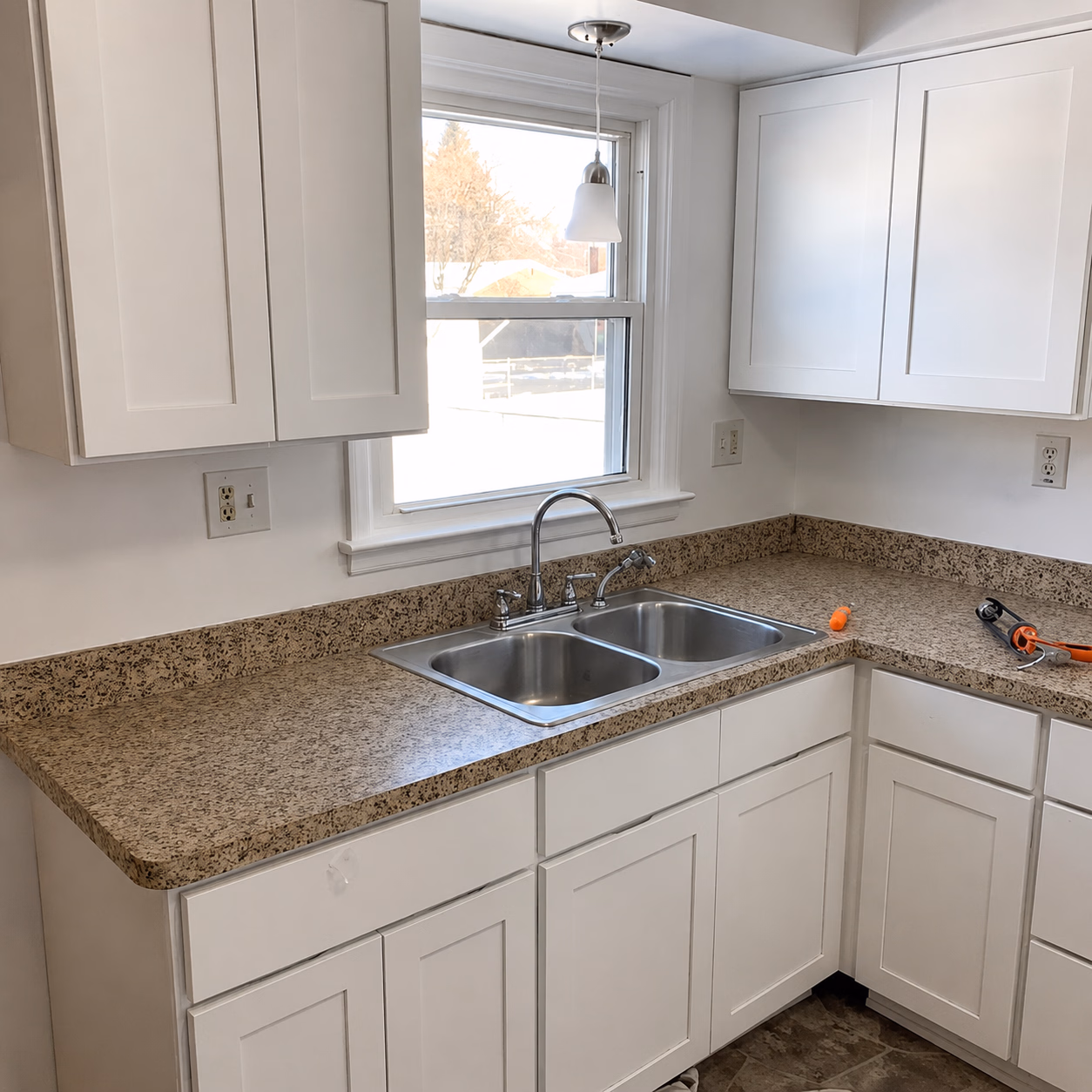 Clean kitchen corner with white cabinets, granite countertop, double stainless steel sink, and window above sink.