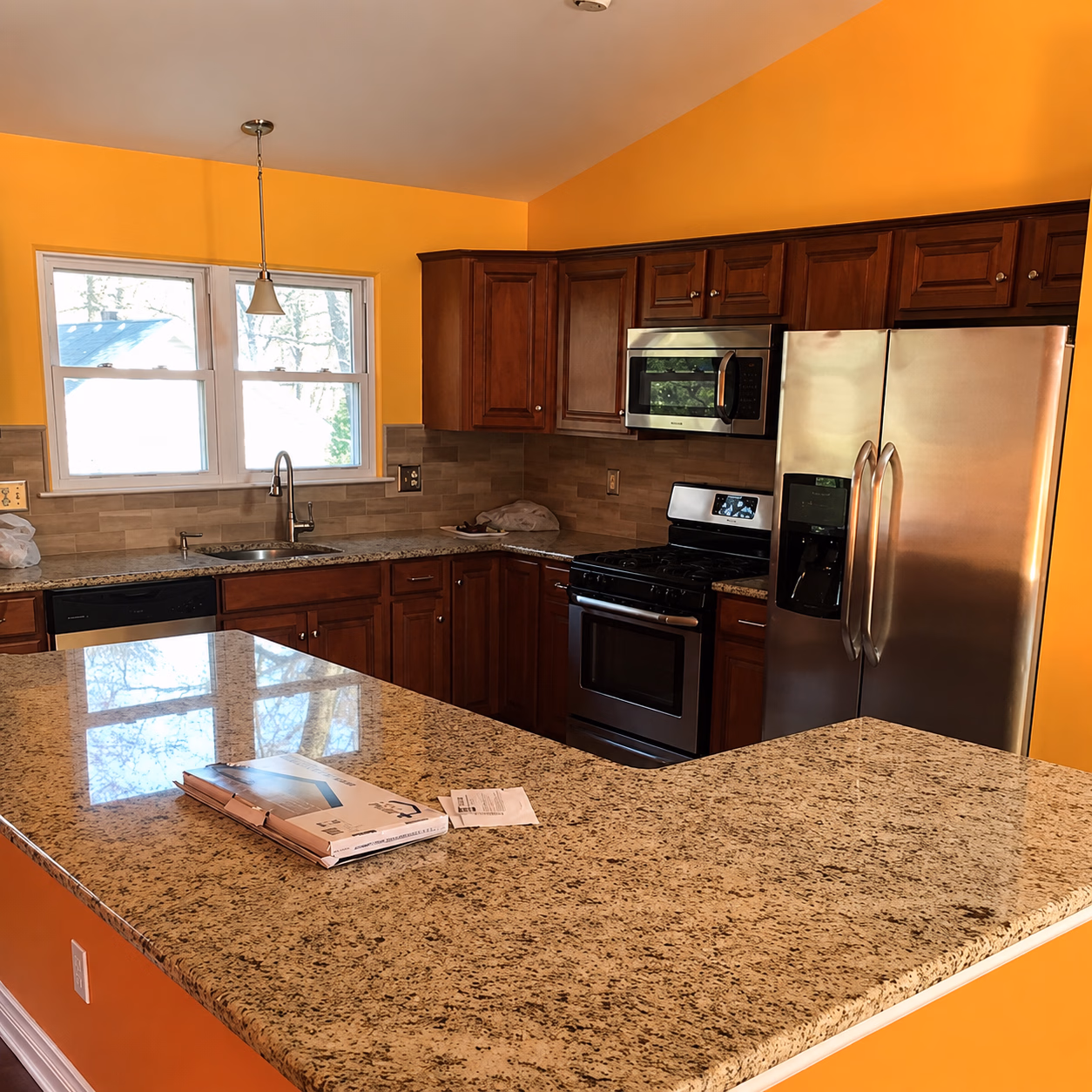 Modern kitchen with granite countertops, wooden cabinets, stainless steel appliances, and bright yellow walls.