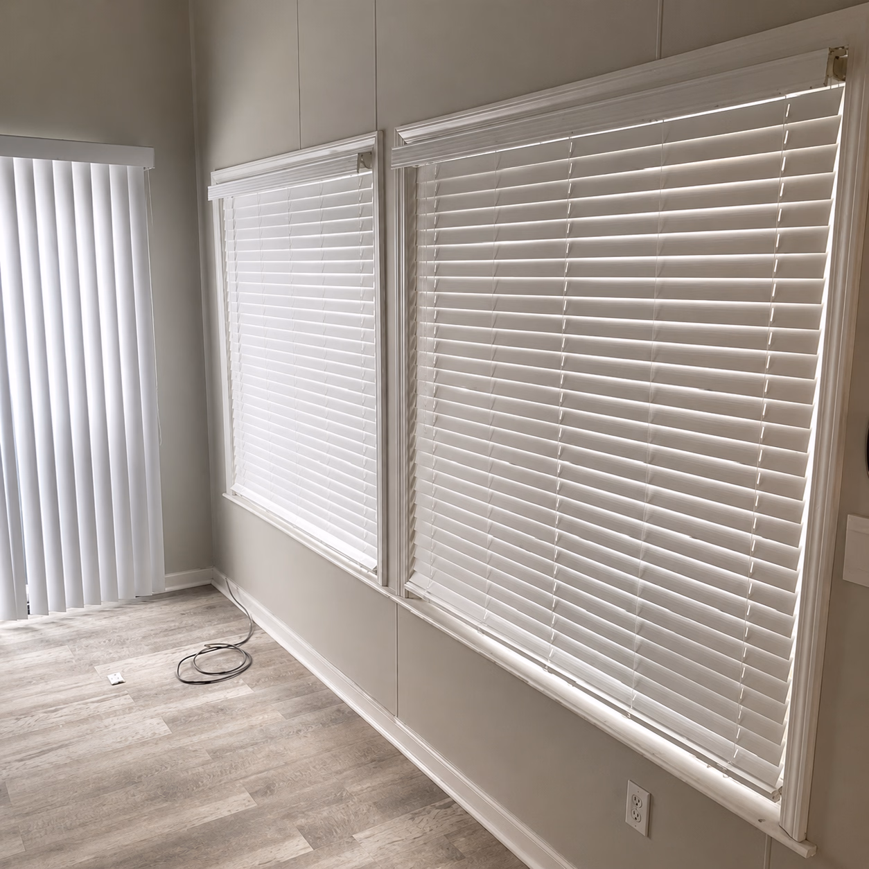 Room corner with two windows covered by white horizontal blinds and vertical blinds on a sliding door.