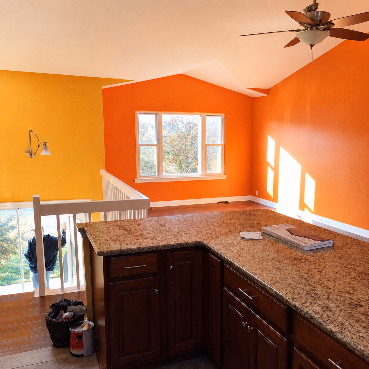 Bright kitchen with granite counter, dark wood cabinets, orange and yellow walls, and a ceiling fan.