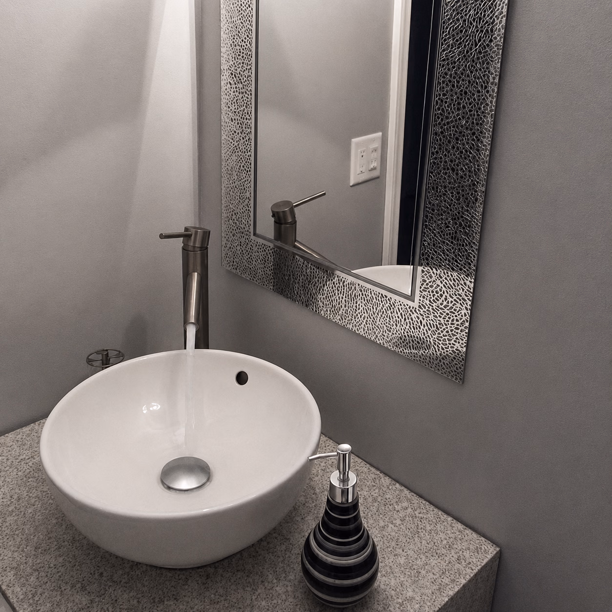 Modern bathroom sink with running faucet, round white basin, soap dispenser, and textured rectangular mirror.