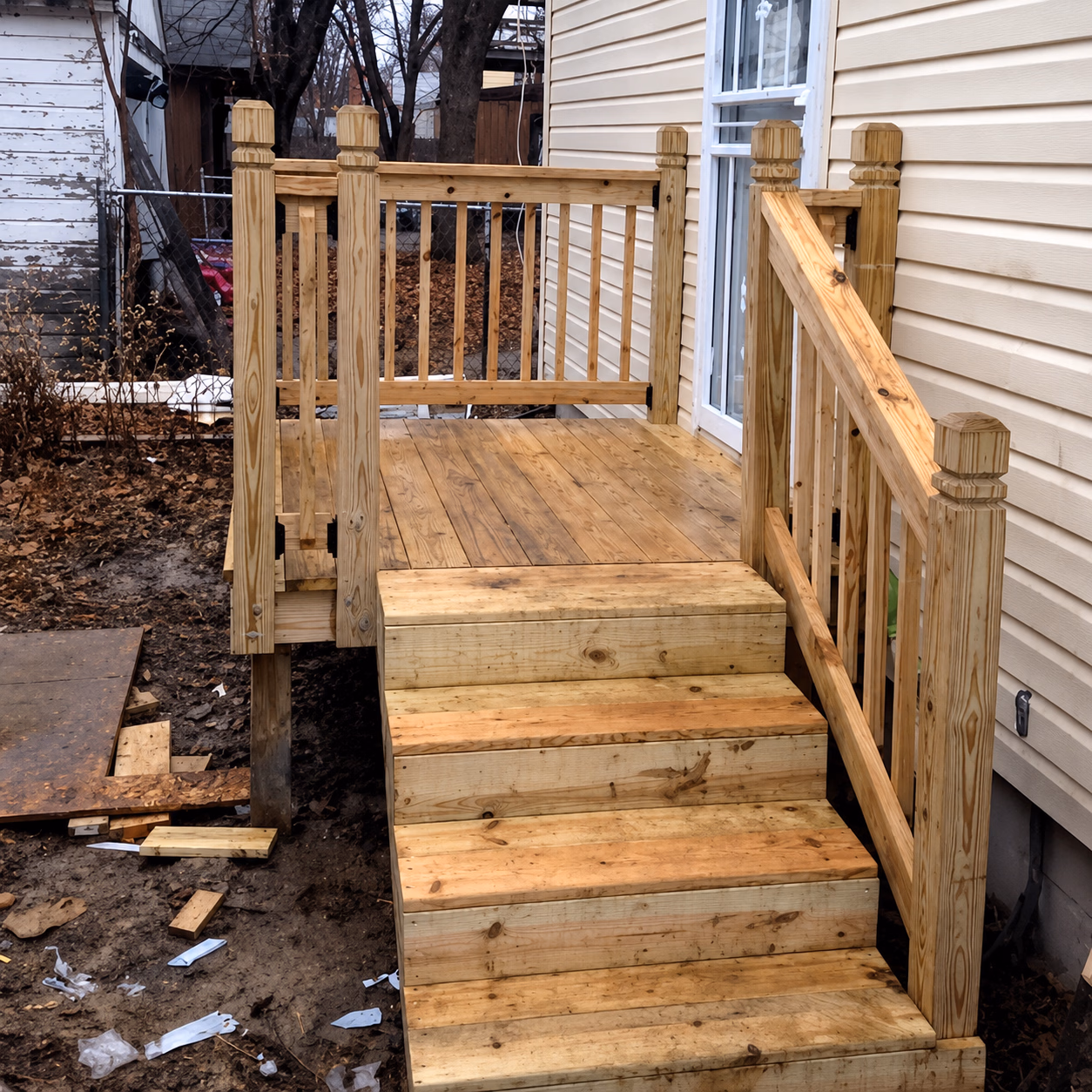 Newly built wooden porch and stairs with railings attached to a beige-sided house.