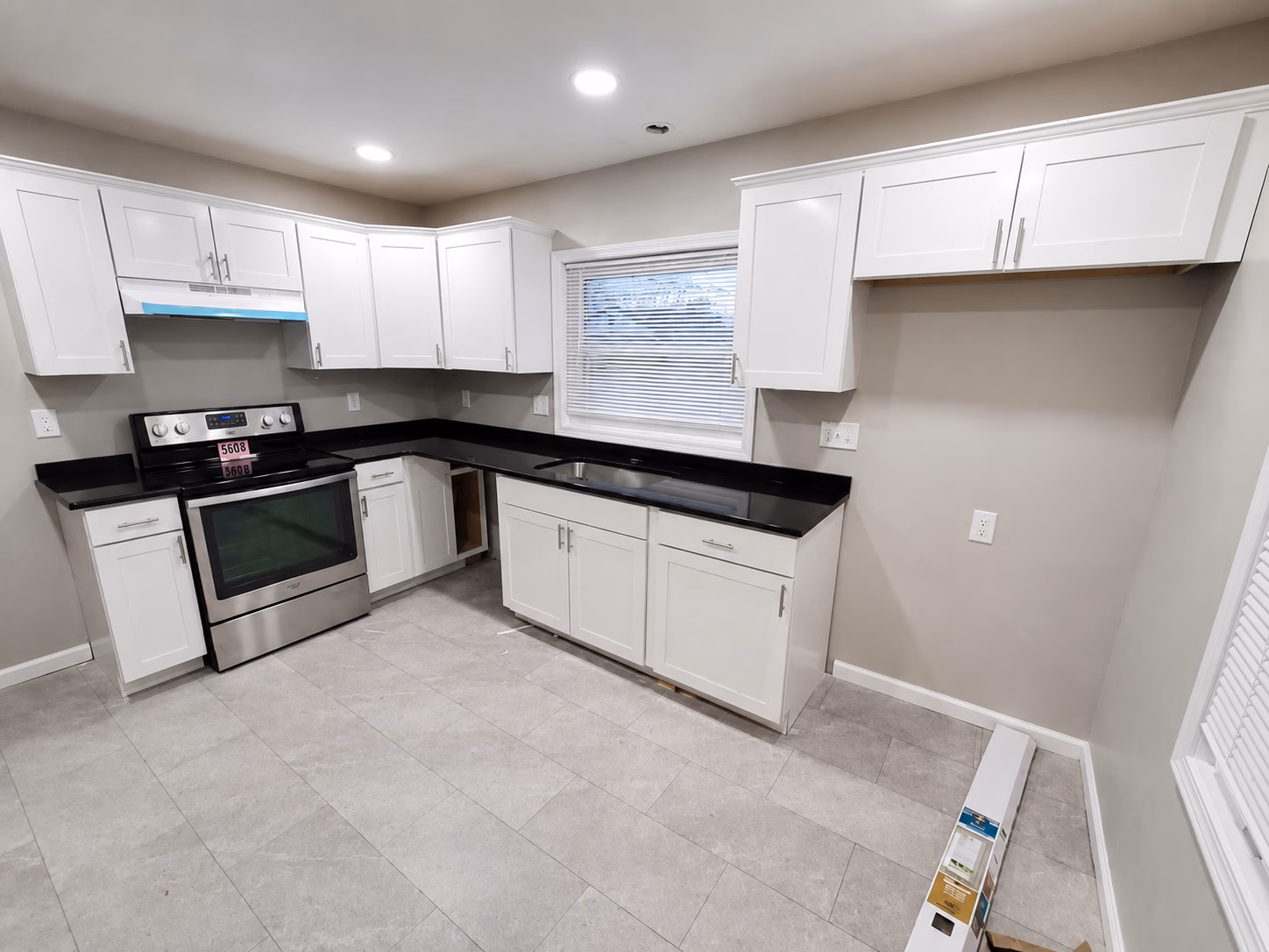 Modern kitchen with white cabinets, black countertops, a stainless steel stove, and tiled floor.
