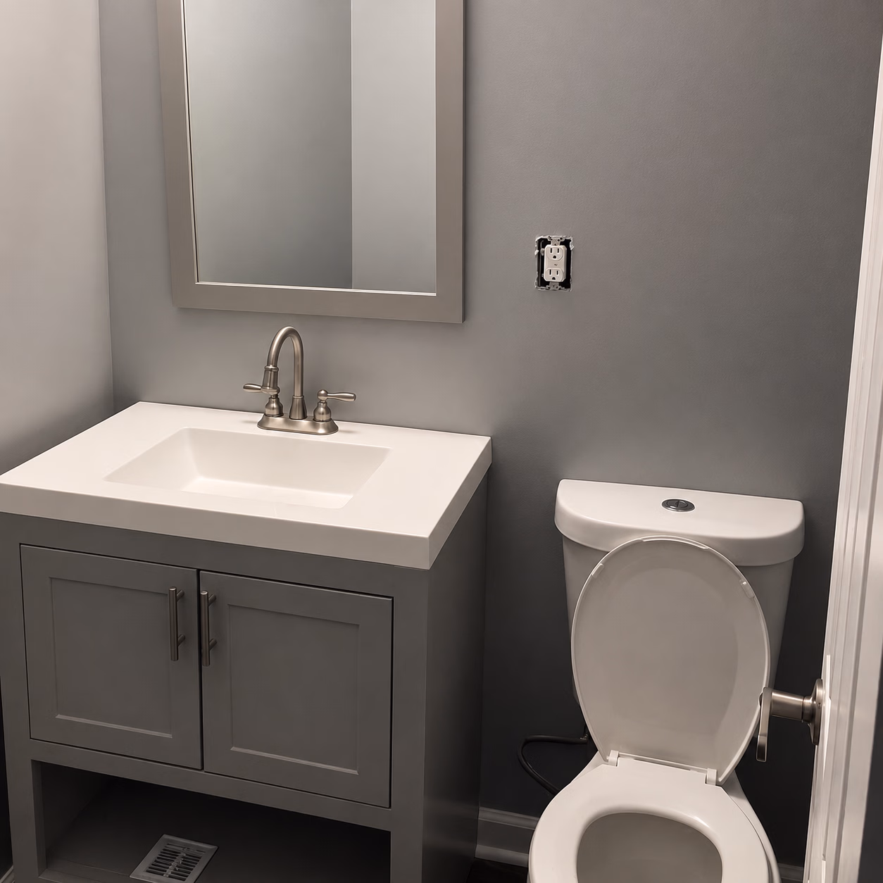 Small bathroom with gray walls, a white sink vanity, and a toilet with an open lid.