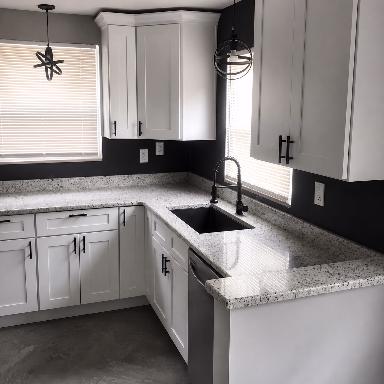 Modern kitchen with white cabinets, black faucet, granite countertops, and two pendant lights over windows.