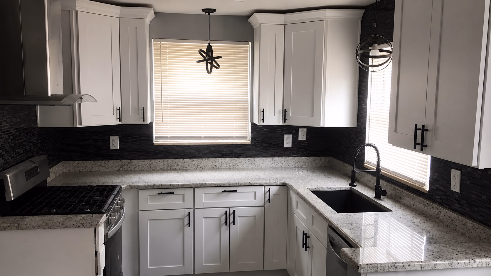 Modern kitchen with white cabinets, granite countertops, black backsplash, black sink, and stainless steel stove.
