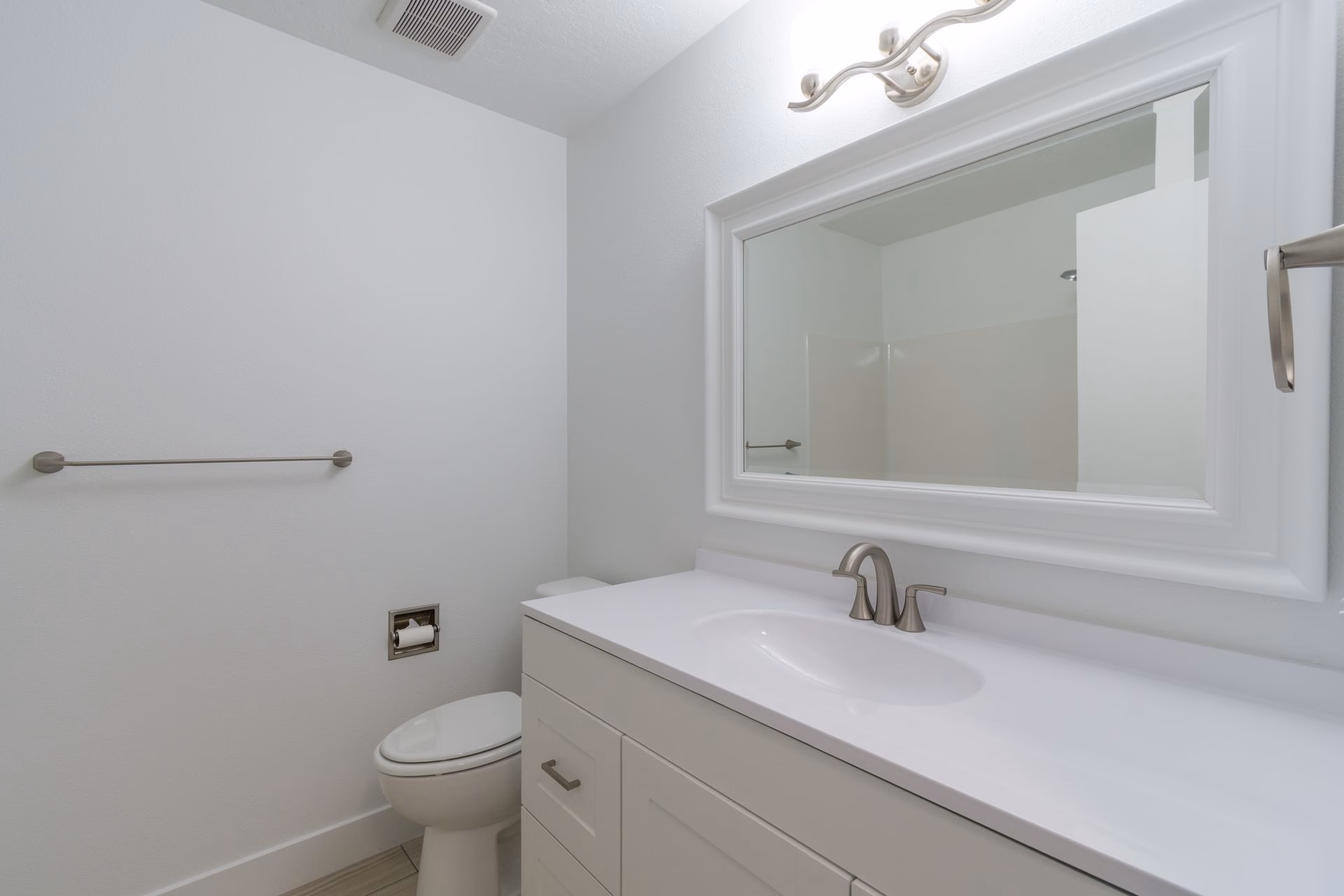 Minimalist white bathroom with vanity, sink, mirror, toilet, and towel rack on wall.